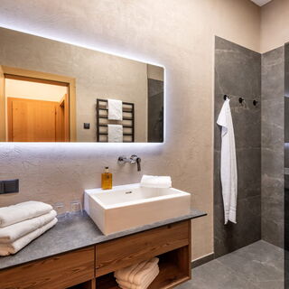 Modernes Badezimmer mit beleuchtetem Spiegel, Waschtisch und Regendusche
